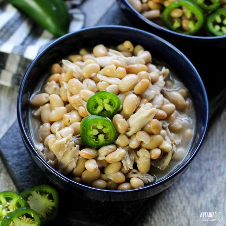 blue bowl with white chicken chili, garnished with 2 slices of jalapeno pepper.