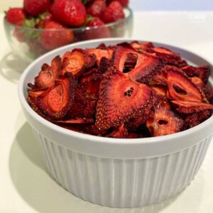 white dish with dried strawberries, fresh berries behind.