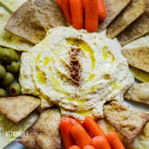 creamy hummus on a platter with pita chips, carrots, and green olives.