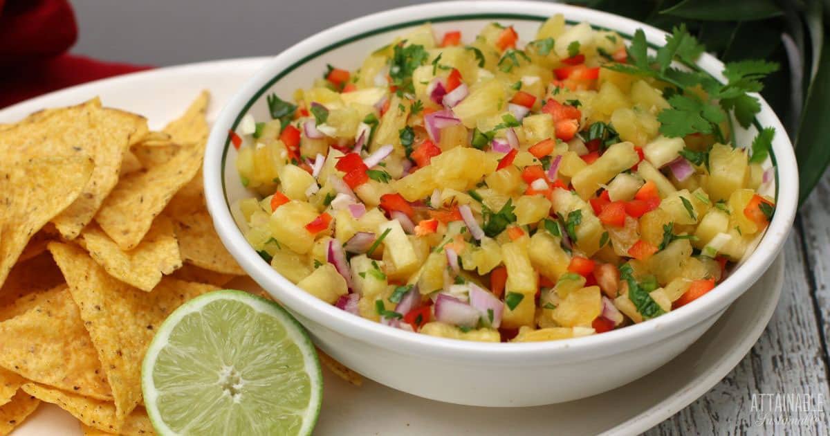 pineapple salsa in a white bowl with chips and a cut lime