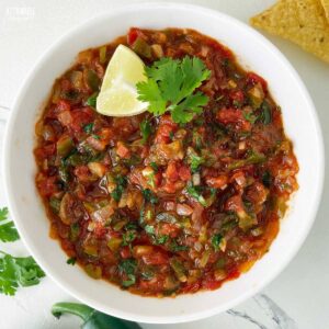 salsa recipe in a bowl, garnished with a wedge of lime and a cilantro leaf.