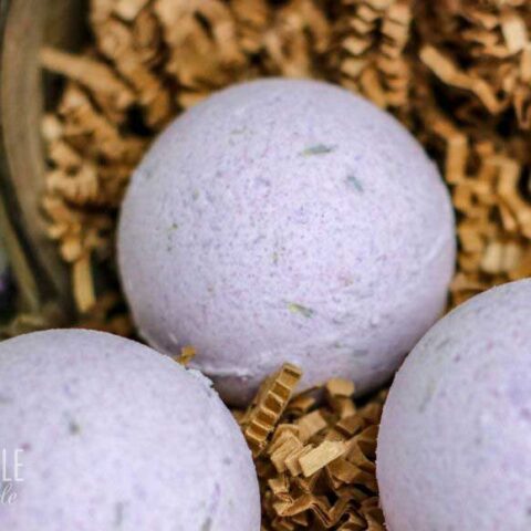 round purple bath fizzy in a basket with shredded paper