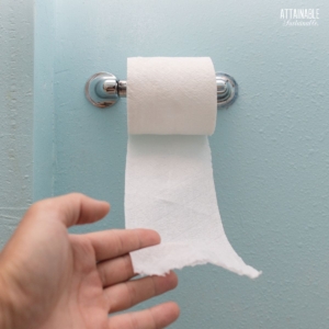 hand pulling toilet paper from a wall mount roll.