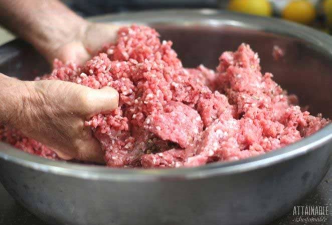 ground pork in a silver bowl, hands mixing it