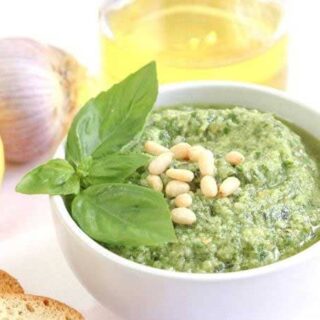 fresh basil pesto in a white dish with basil leaves and pine nuts