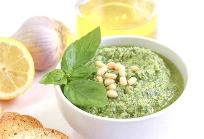 fresh basil pesto in a white dish with basil leaves and pine nuts