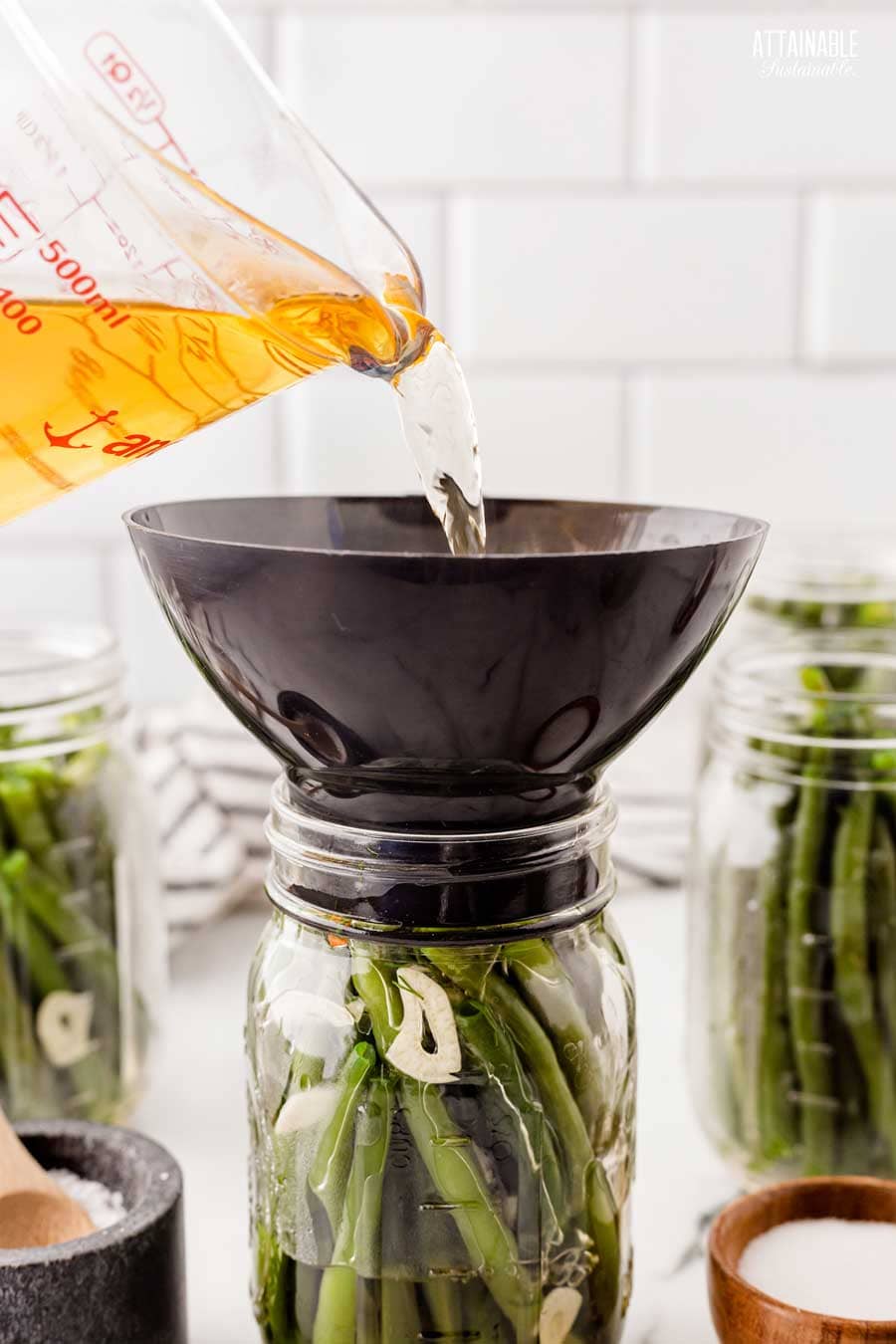 amber liquid poured through a funnel into a mason jar filled with green beans.