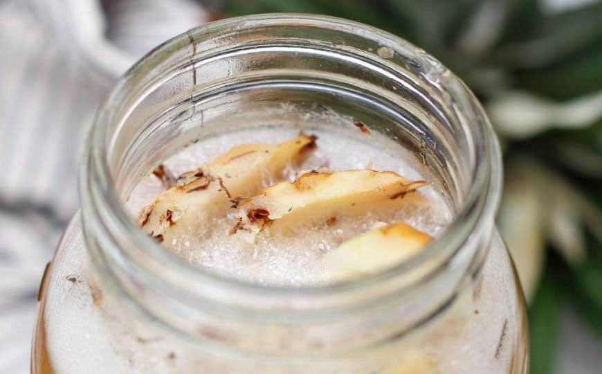 bubbles and pineapple pieces visible in a glass fermentation jar