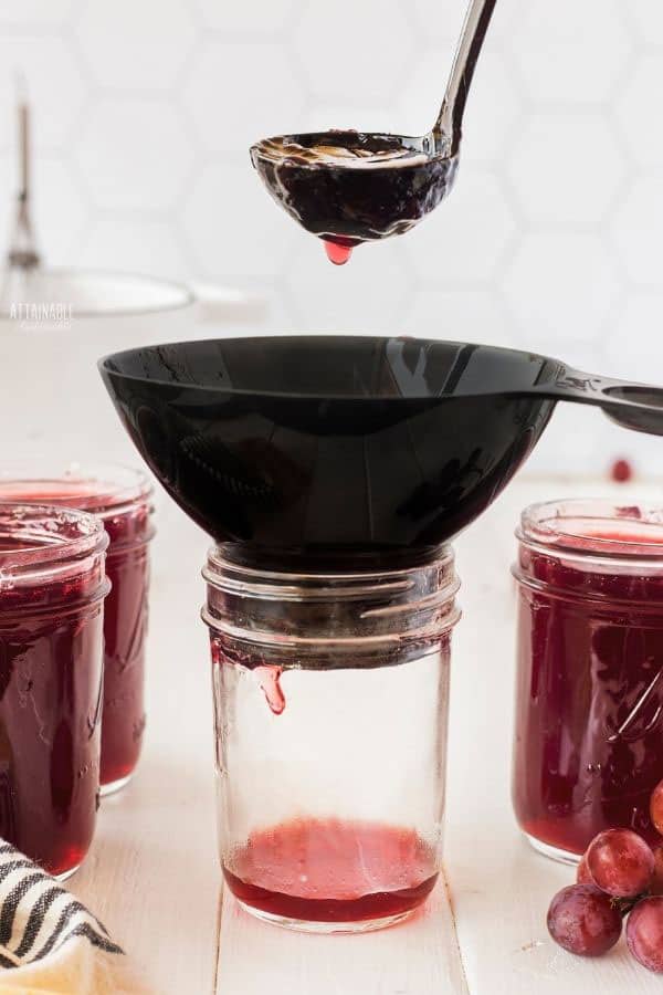 glass canning jar with funnel and ladle of jelly