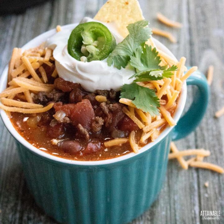 teal cup full of chili topped with shredded cheese, sour cream, and a slice of jalapeno.