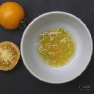 yellow cherry tomatoes one whole, one half, with tomato seeds in a white bowl, all on a black background.