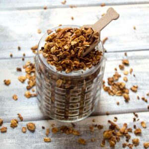 granola in a patterned glass jar with a wooden scoop.