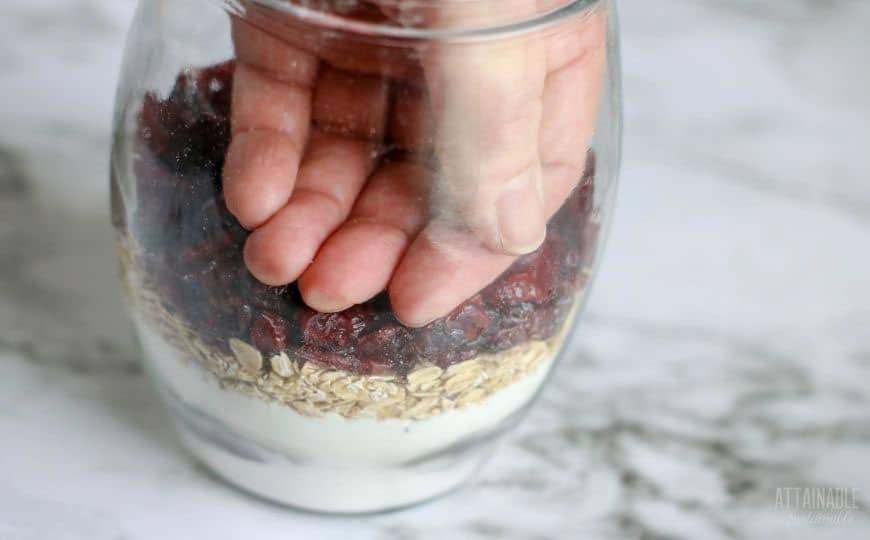 hand in a glass jar, pressing cookie ingredients
