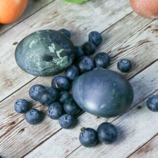 easter eggs dyed dark blue alongside blueberries