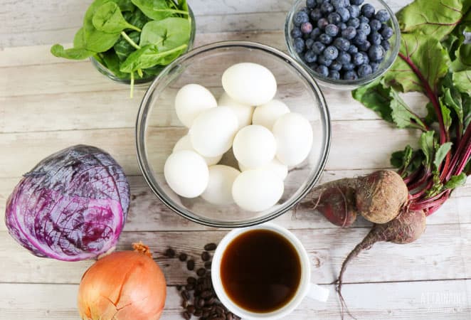 bowl of hard boiled eggs with the ingredient to Dye Easter Eggs Naturally (red cabbage, onion, spinach, coffee, blueberries, beets)