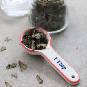 glass jar of dried basil leaves, with some in a ceramic tablespoon measure.