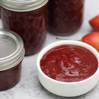 red ketchup in a white dish with canning jars surrounding it