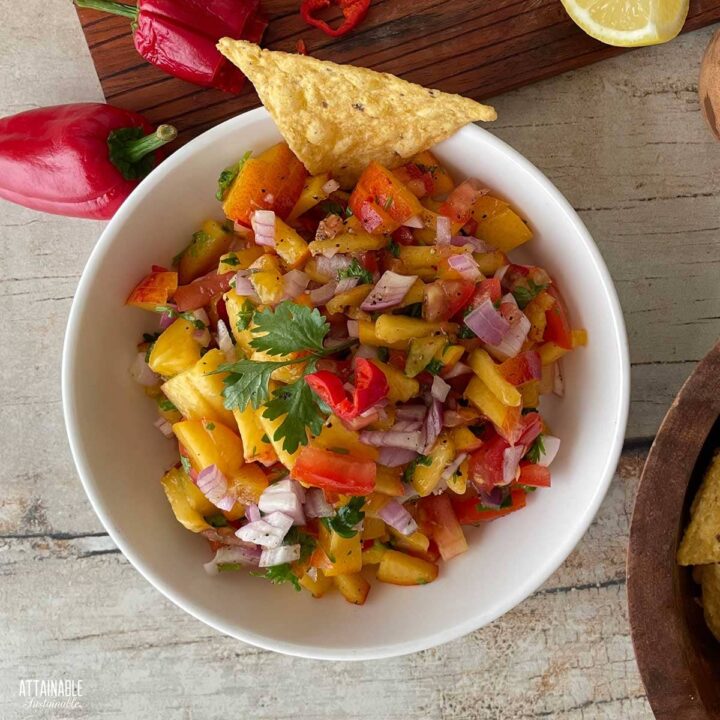 bowl of fresh peach salsa from above, red habanero peppers in the background.