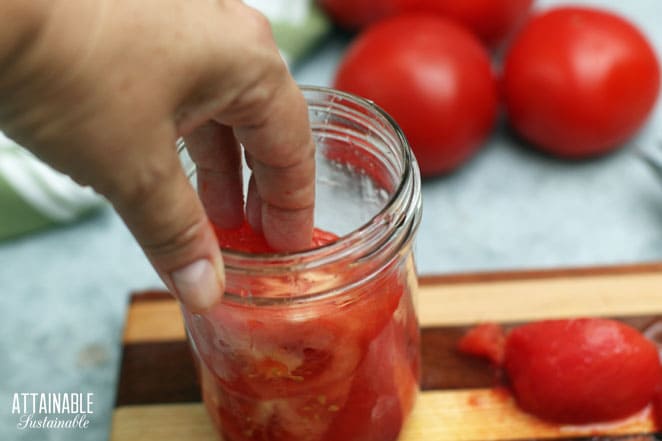 hand pressing tomatoes into a glass jar