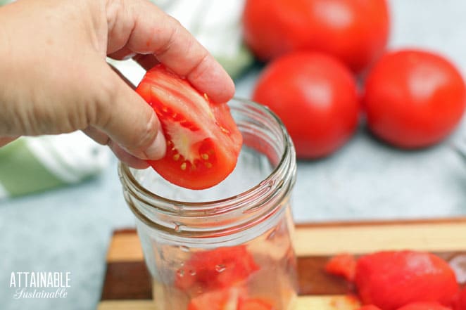 hand dropping a chunk of raw tomato into a jar