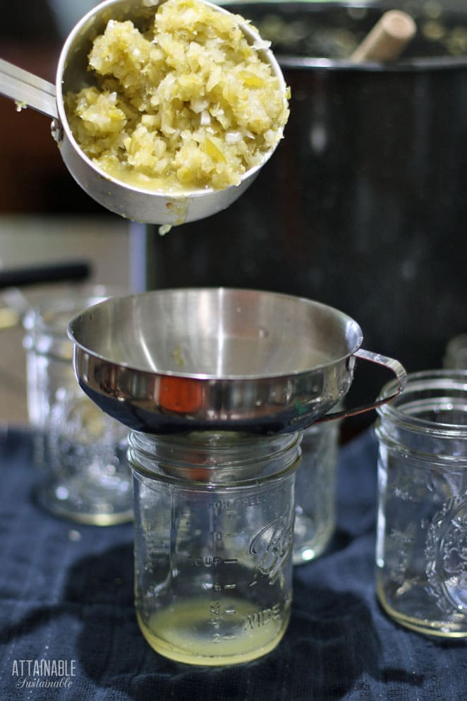 scooping chow chow into a glass jar through a silver canning funnel