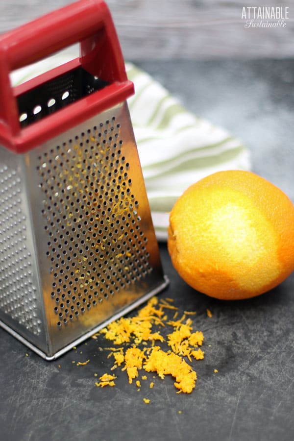 box grater with orange peel on black board