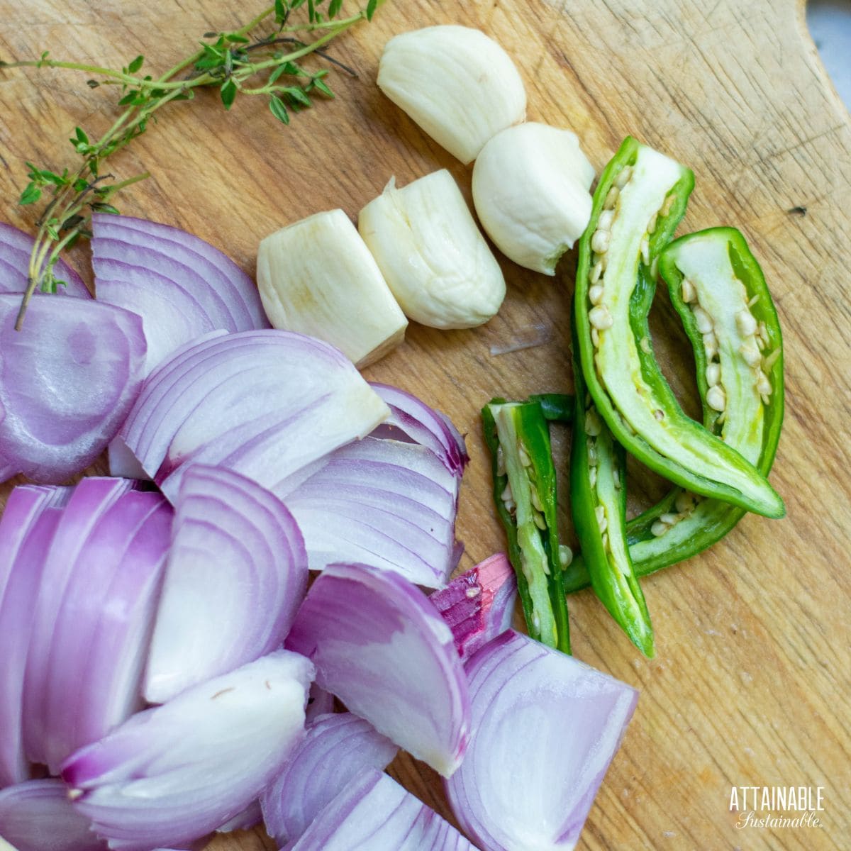 sliced red onions, jalapeno, fresh garlic, fresh thyme on a cutting board.