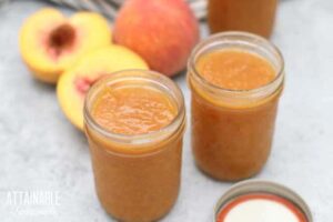 jars of peach butter with lids off, peaches behind