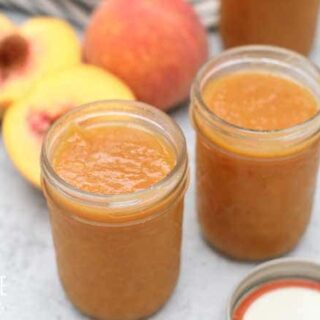 jars of peach butter with lids off, peaches behind