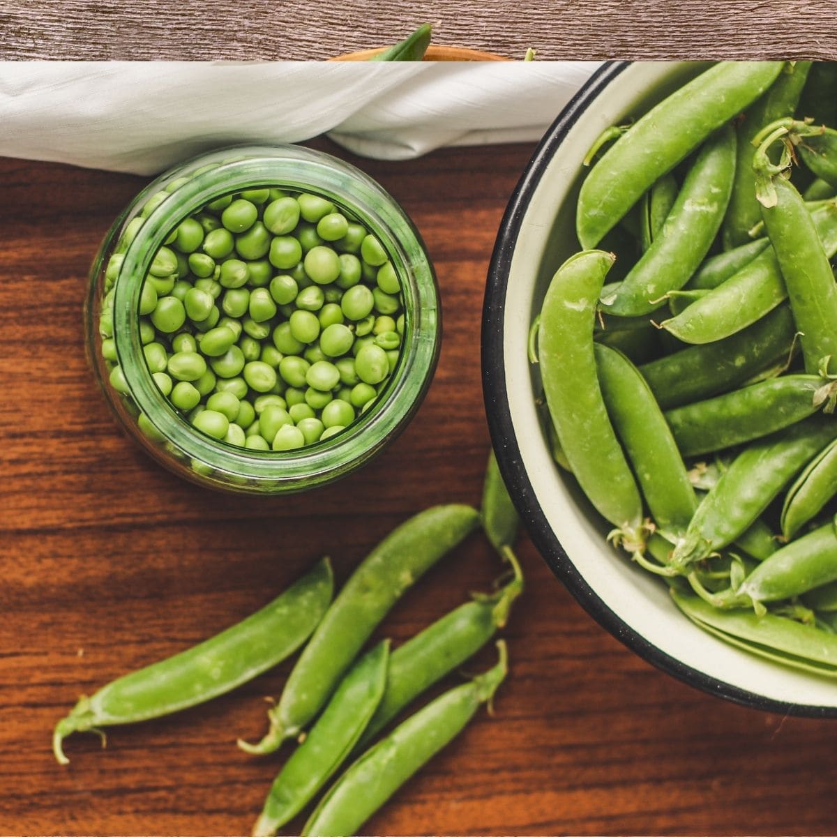 Peas in pods in a bowl and on cutting board, and shelled peas in a jar. 
