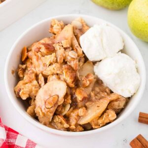 bowl of pear crisp topped with scoops of vanilla ice cream.