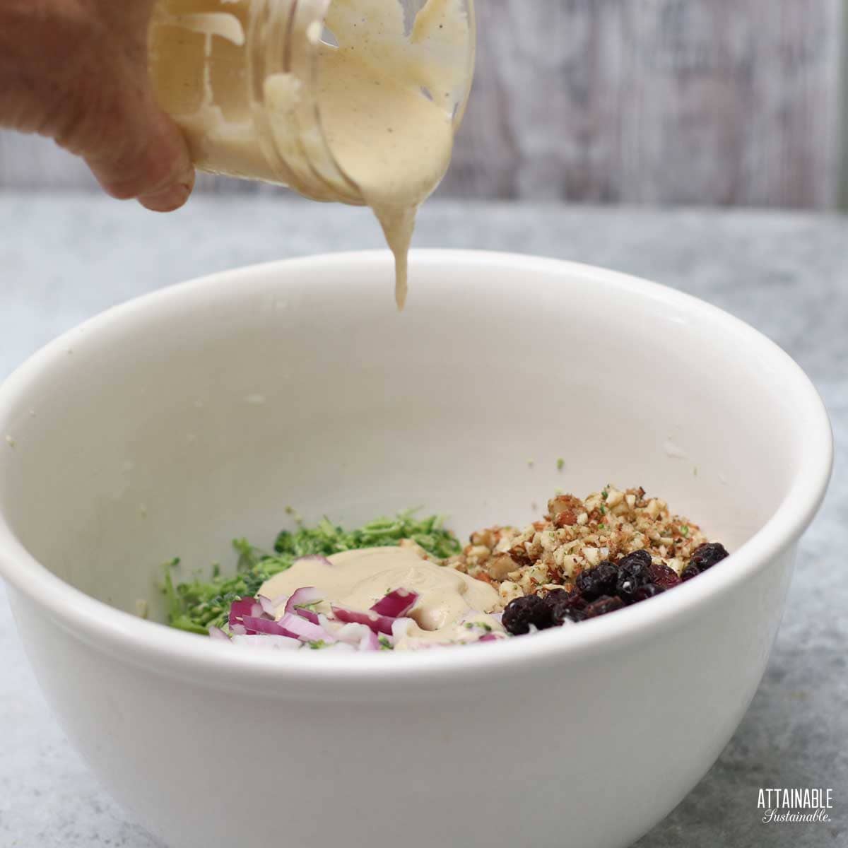 hand pouring dressing into a bowl of ingredients.