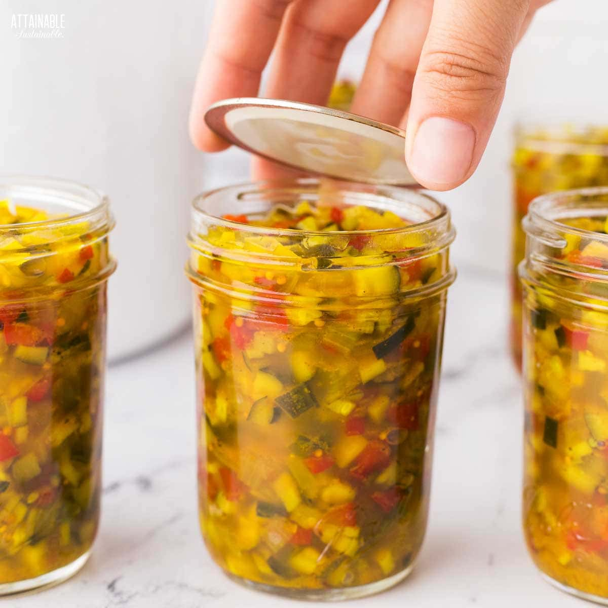 hand placing a canning lid on a jar.