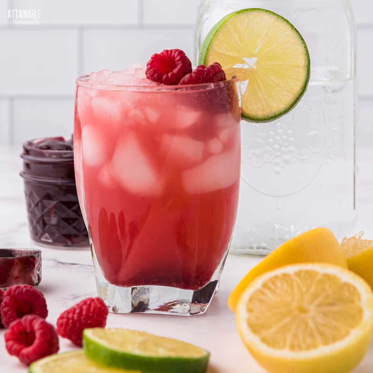 jam seltzer in a glass garnished with raspberries and limes.