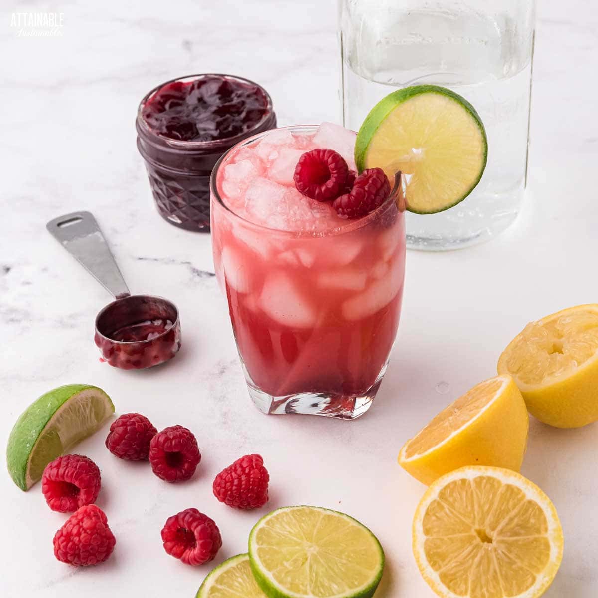 glass of red drink amid fresh limes, lemons, berries.