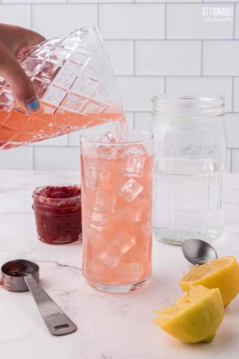 hand pouring pink liquid in to a glass of ice.