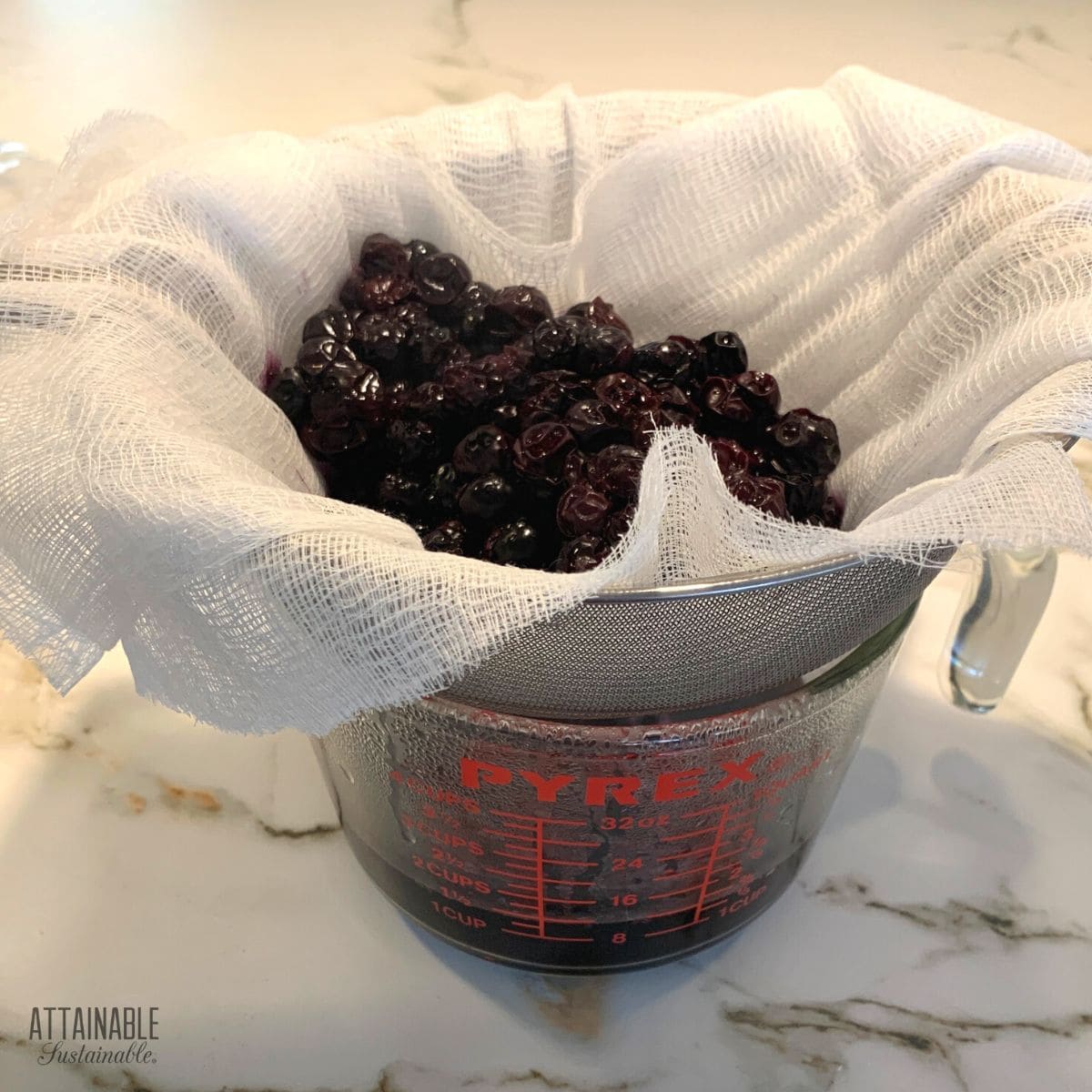 berries draining in cheesecloth lined sieve.