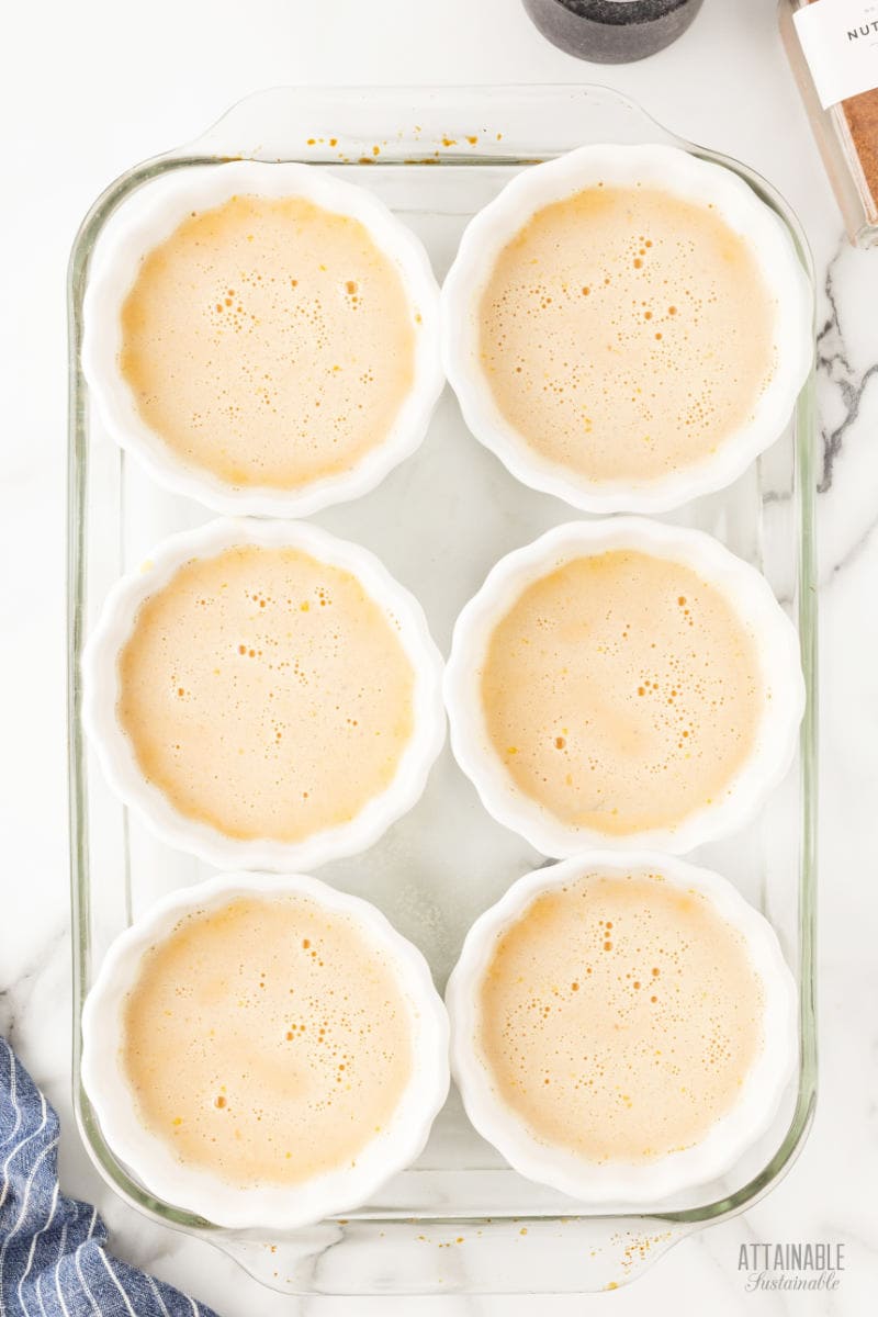 pumpkin custard in 6 white ramekins sitting in a glass dish.
