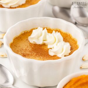 baked pumpkin custard cup in a white scalloped dish, topped with whipped cream.