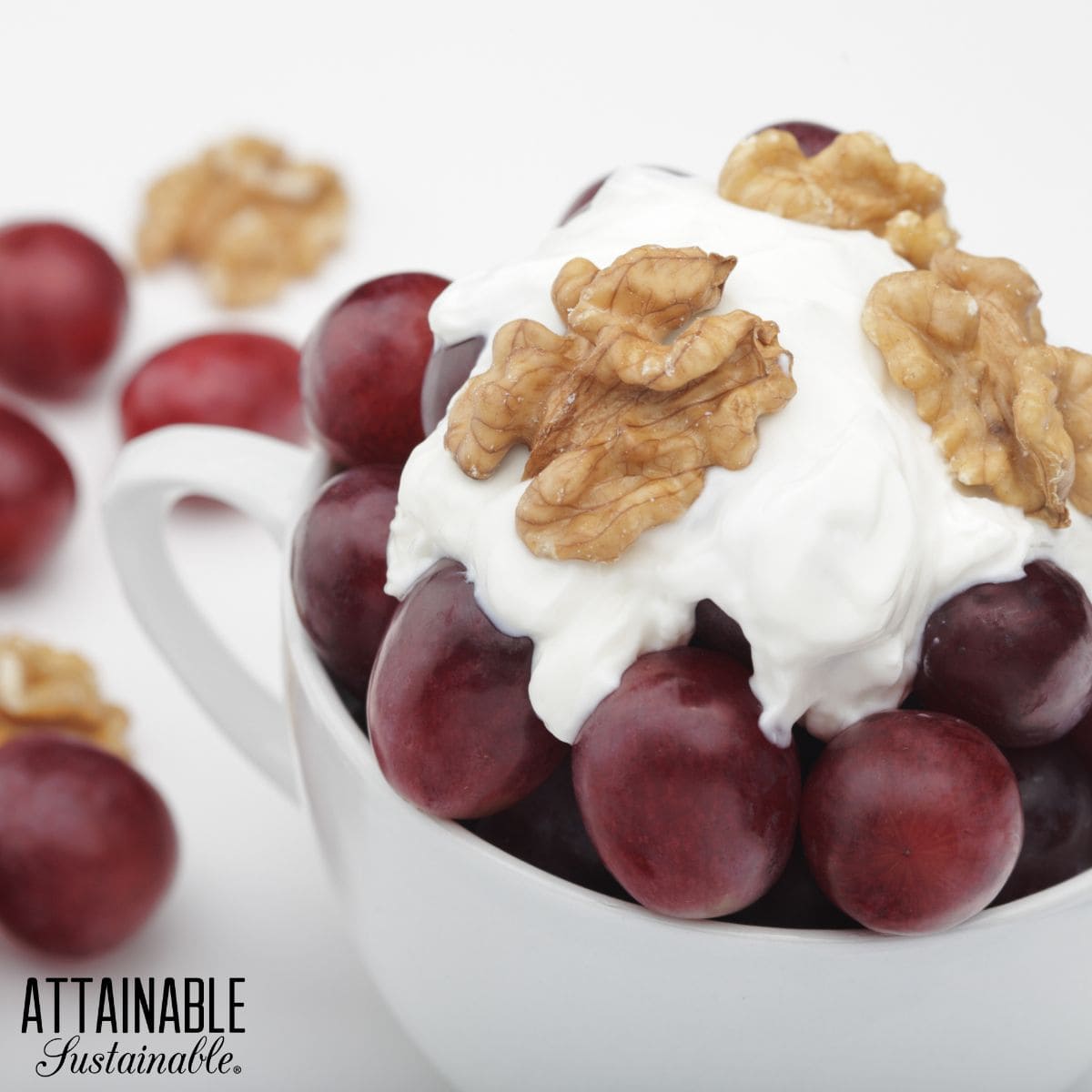 Red grapes in a white mug topped with yogurt and walnuts. 