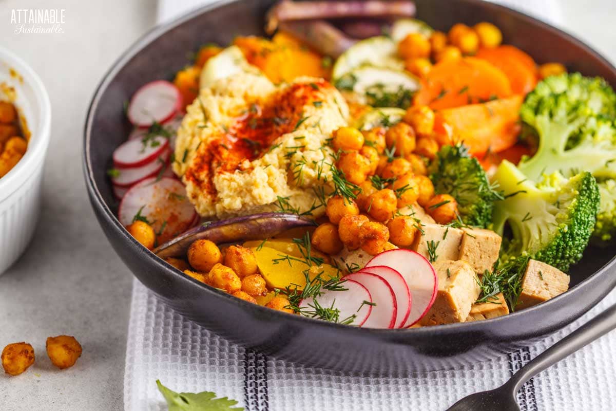 brown bowl with hummus, radish slices, broccoli, and chickpeas.