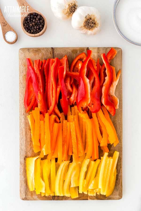 sliced red, orange, and yellow peppers on a cutting board.