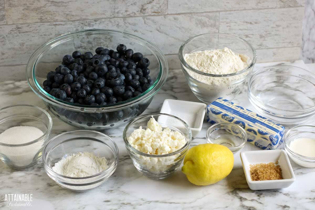 Measured ingredients for blueberry galette in different sized bowls on a grey countertop. 