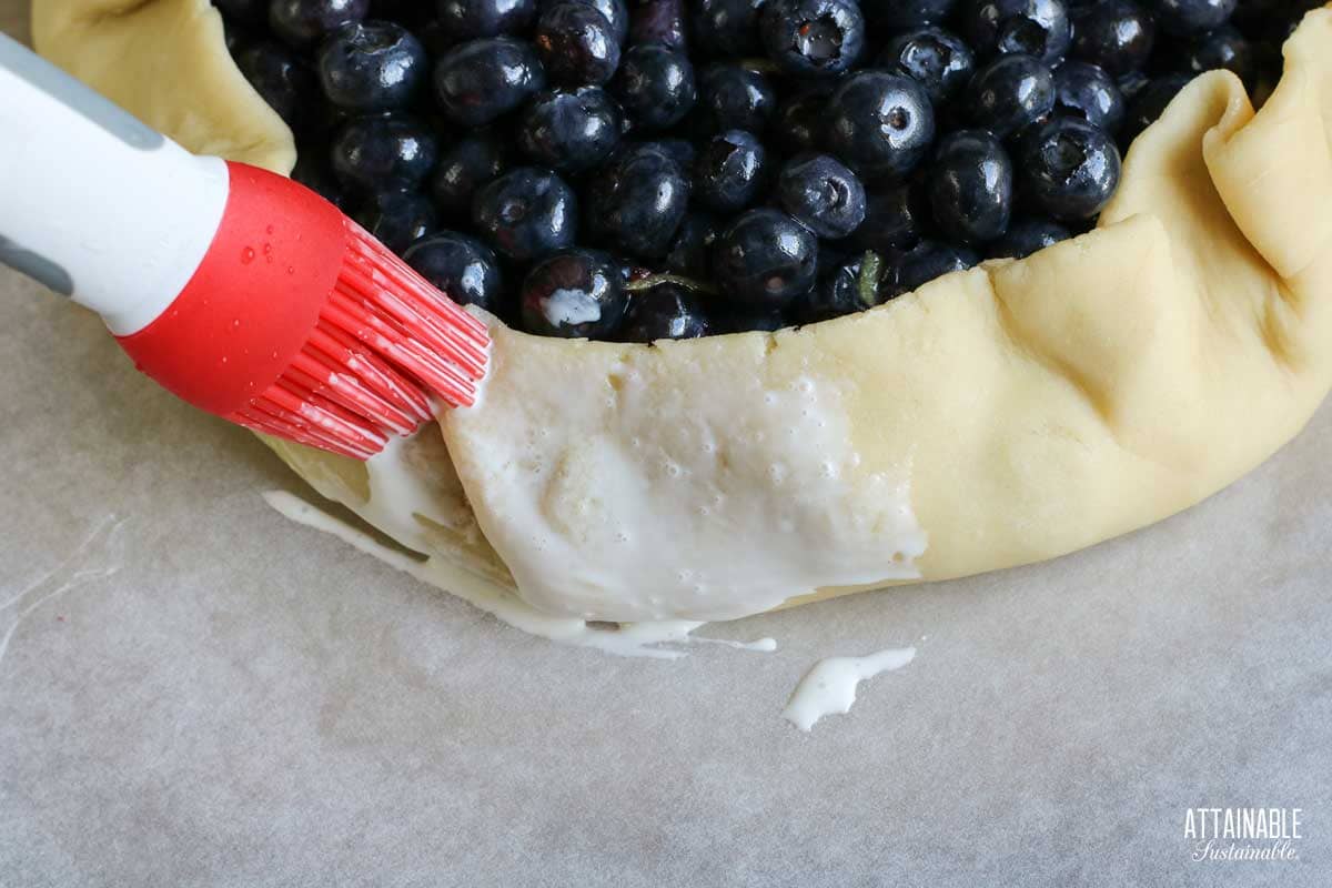 A silicon brush on the edge of the uncooked crust dough, brushing cream on it. 