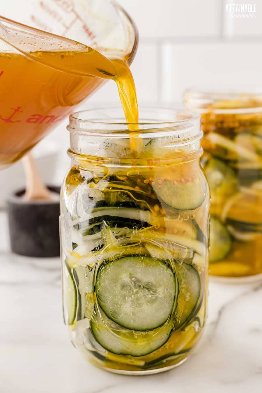 measuring cup pouring brine over cucumbers in a jar.