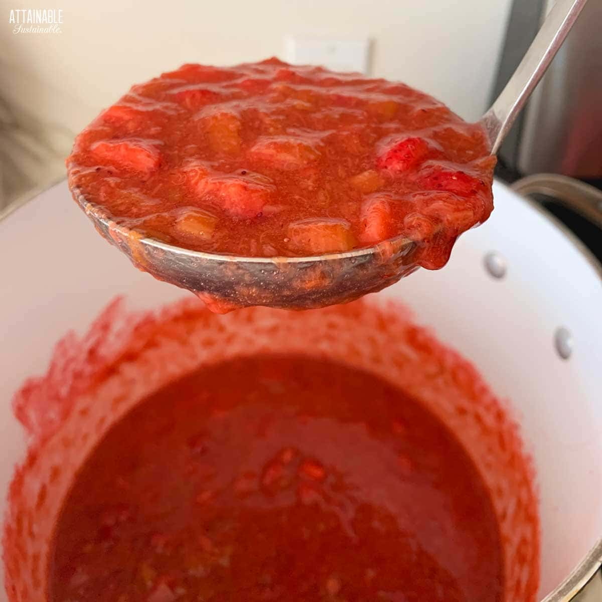 strawberry rhubarb jam in a pot, with a ladle of the jam above.