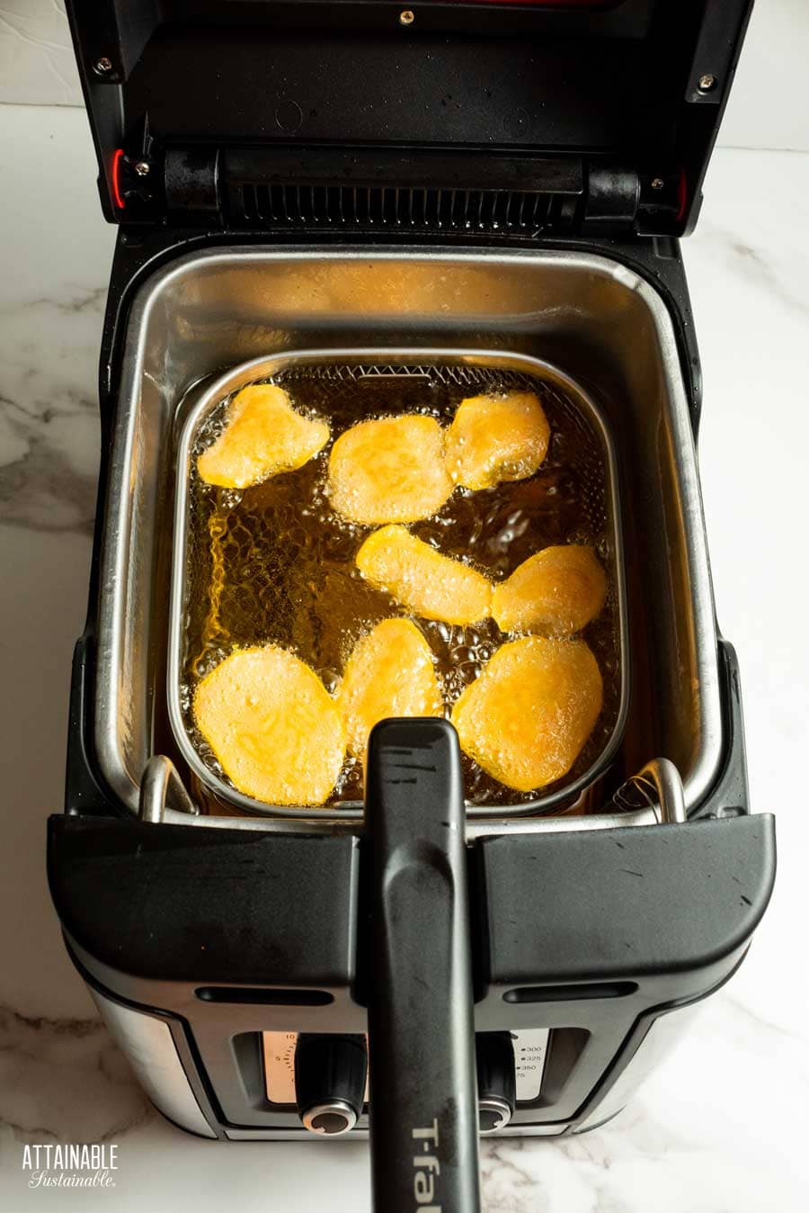 Sweet potato slices in a deep fryer pan and oil bubbling. 