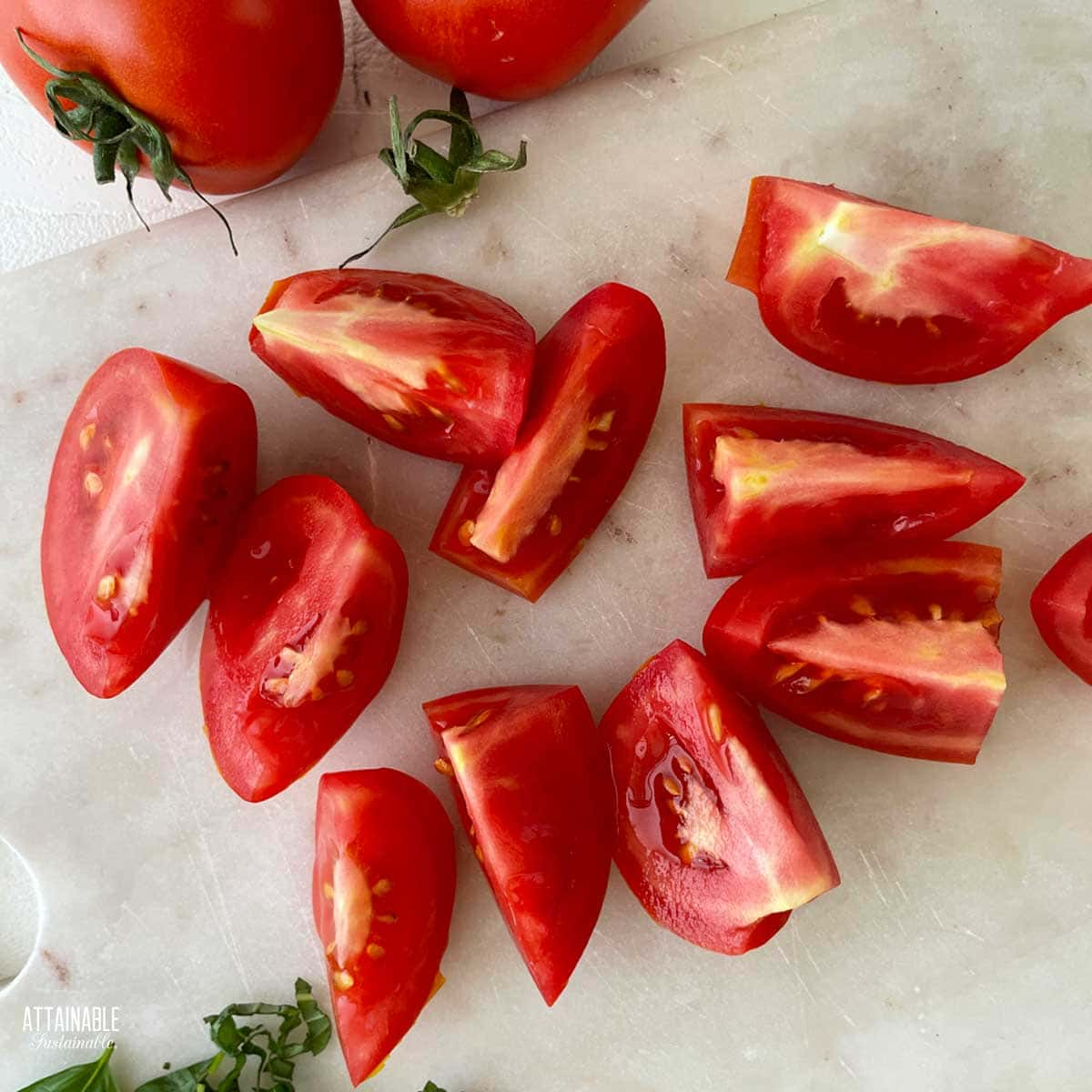 Sliced tomatoes on a white surface, with a couple of whole tomatoes to the top.