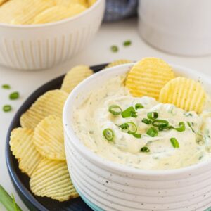 green onion dip in a white bowl, served with ruffled chips.