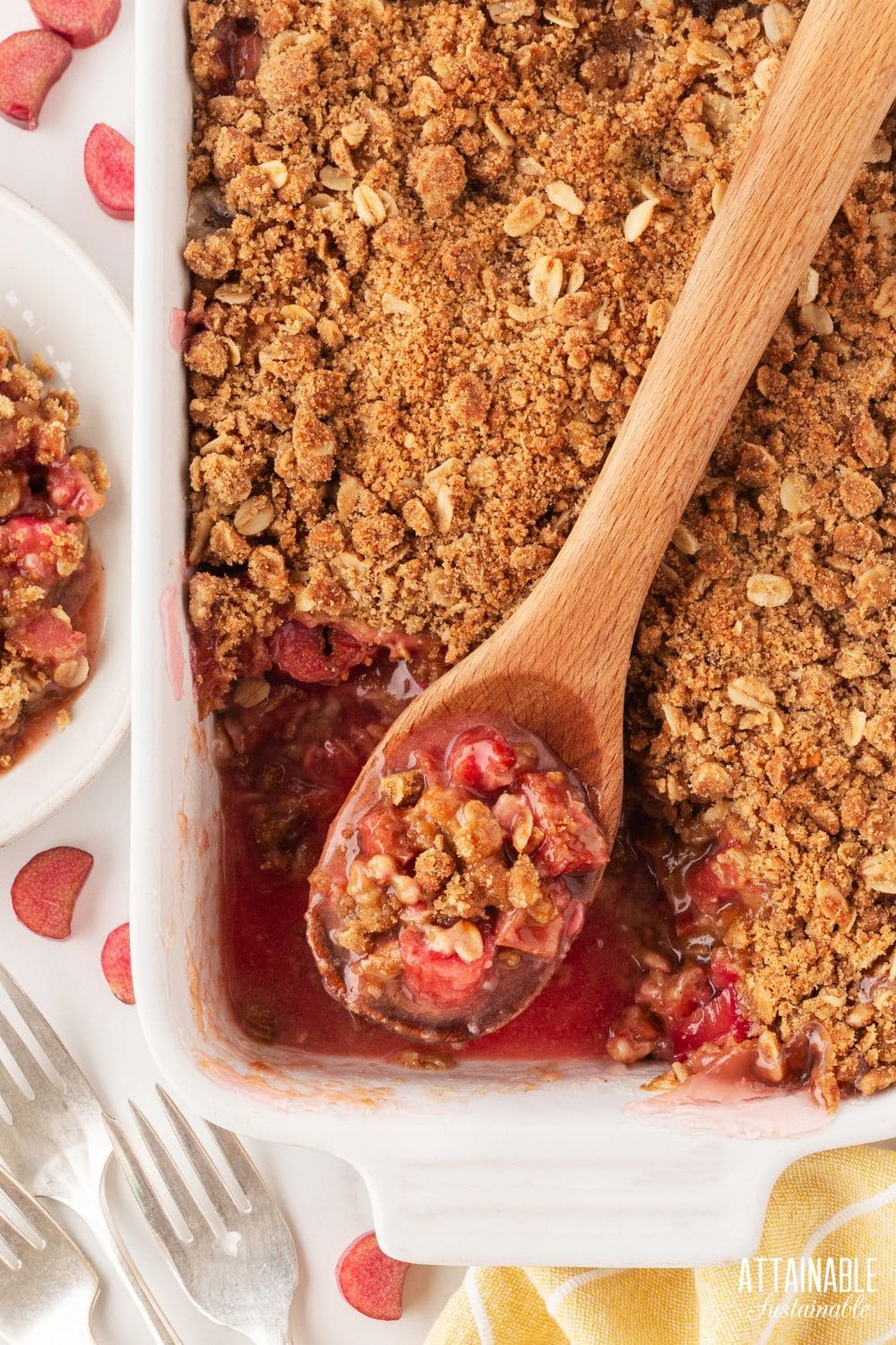 rhubarb crisp in a white baking dish with a serving scooped out in a wooden spoon.